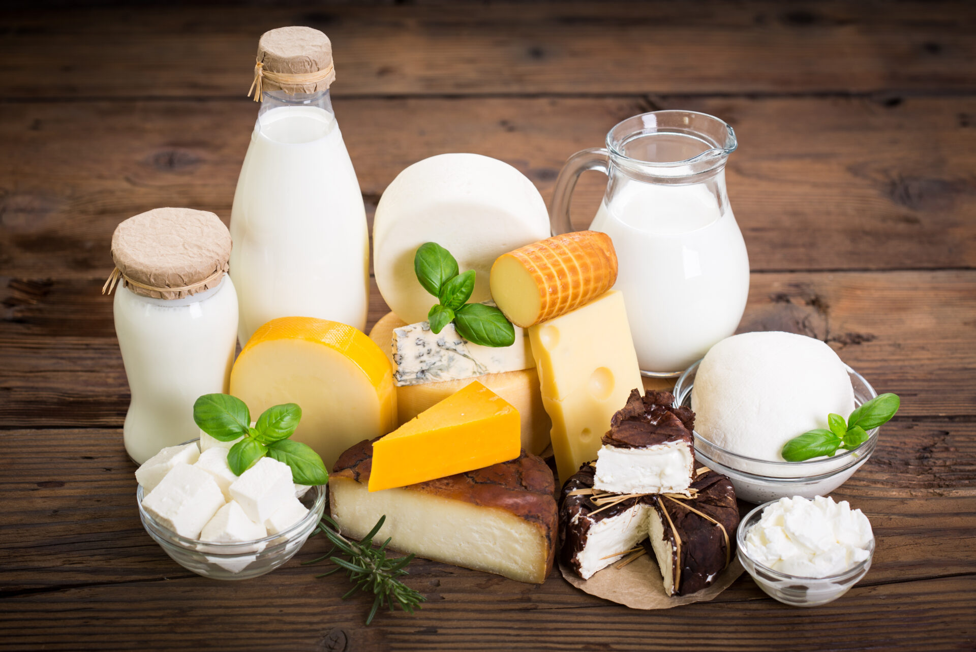 Display of several milk products on a wooden surface - bottles of milk, creams, and cheeses.