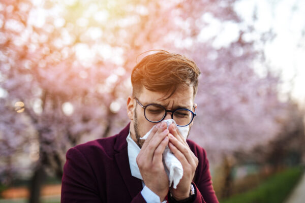 Young businessman sneezing in the park.